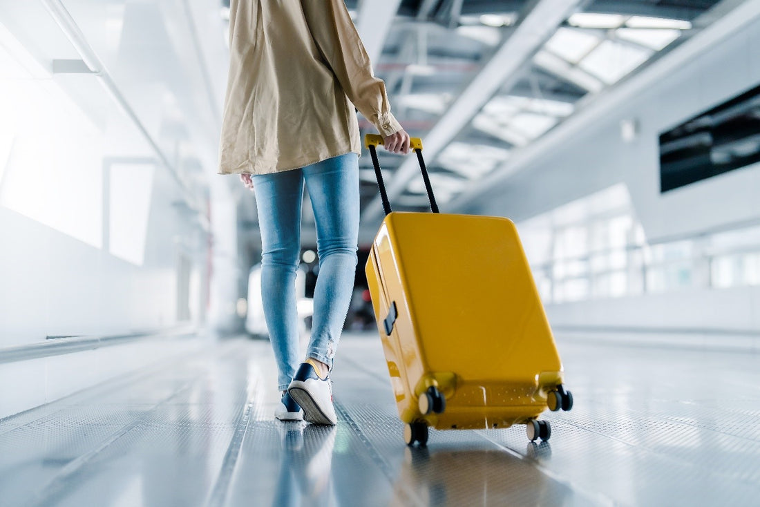 A person walking down an airport terminal rolling a yellow suitcase behind them