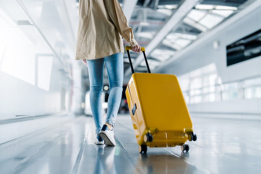 A person walking down an airport terminal rolling a yellow suitcase behind them