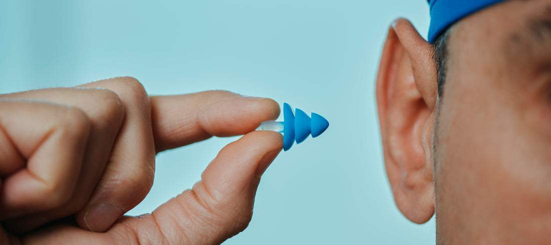 A person wearing a swim cap inserts a pool ear plug into their ear