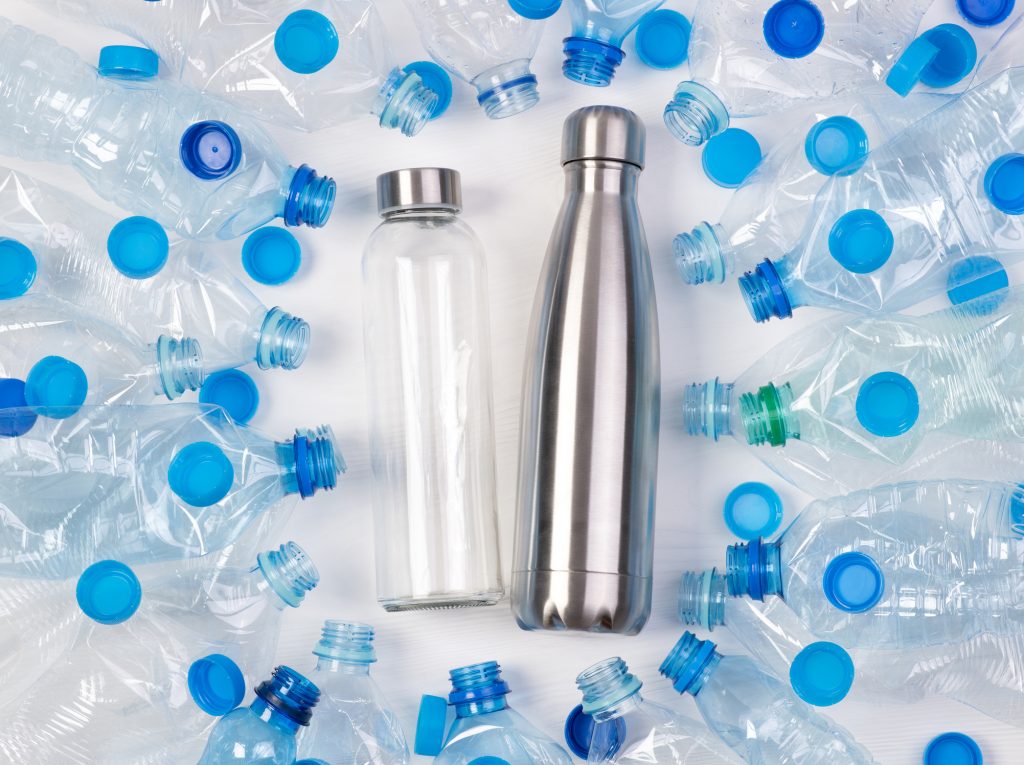A metal water bottle and glass water bottle lying down and surrounded by plastic water bottles