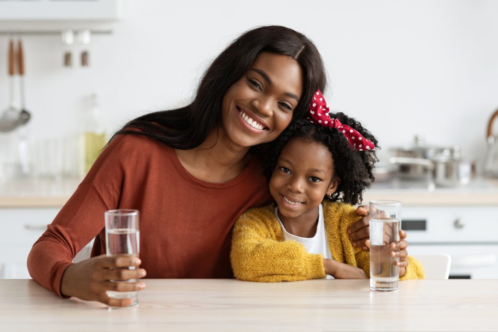 A mother and daughter sit at their family kitchen table and drink clear water together