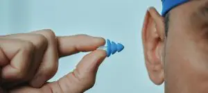A person wearing a swim cap inserts a pool ear plug into their ear
