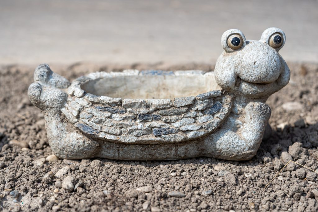 A humorous concrete frog statue with a smile, wide eyes, and shaped like a bowl