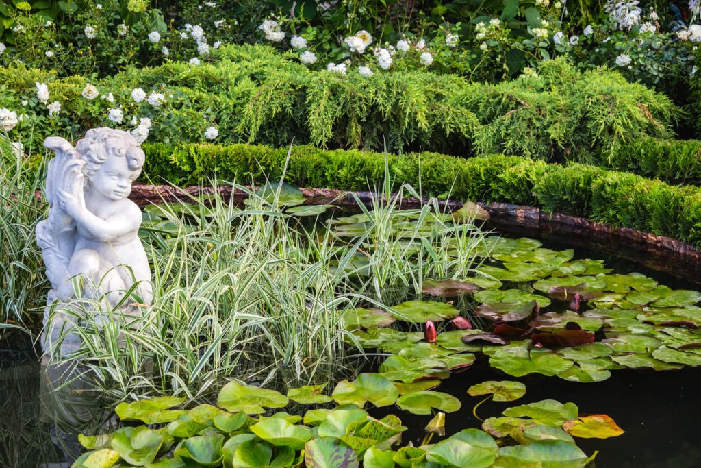 A concrete garden statue of a cherub set artistically in a garden pond