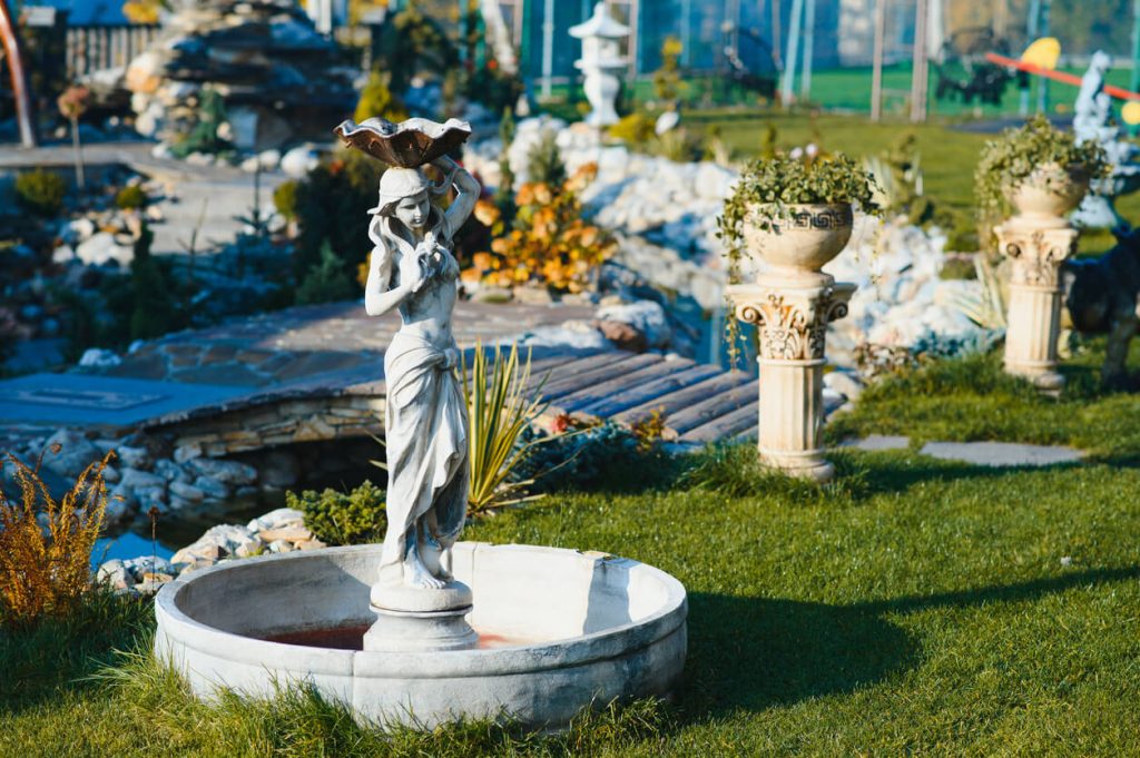 A park garden fountain with a woman statue fountain and concrete columns with flower pots