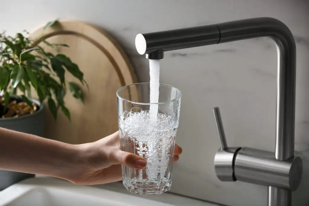 Someone pours clean water into a glass from their kitchen sink, thanks to their whole house UV water filter